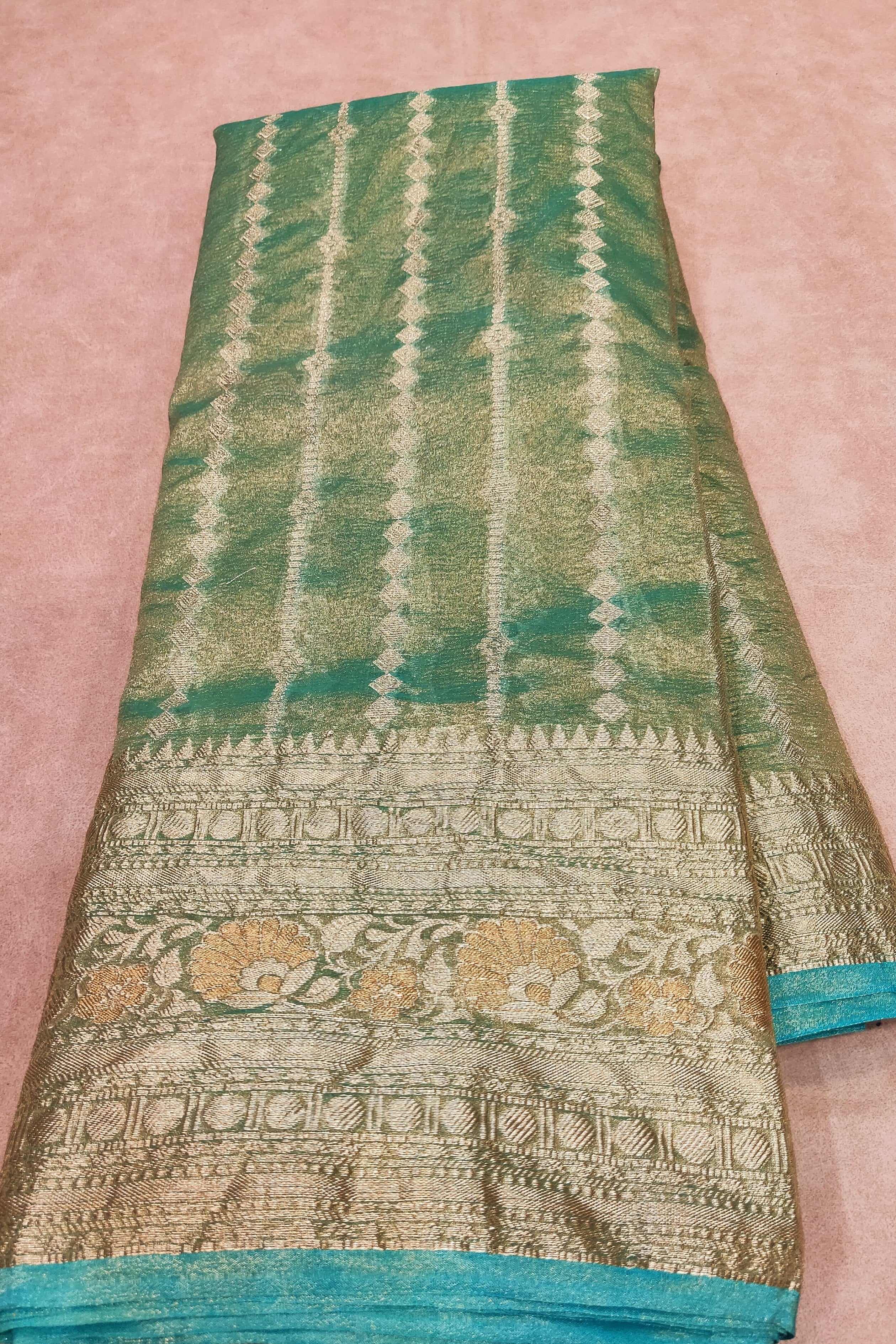 Green and gold patterned fabric held by a hand on a pink background