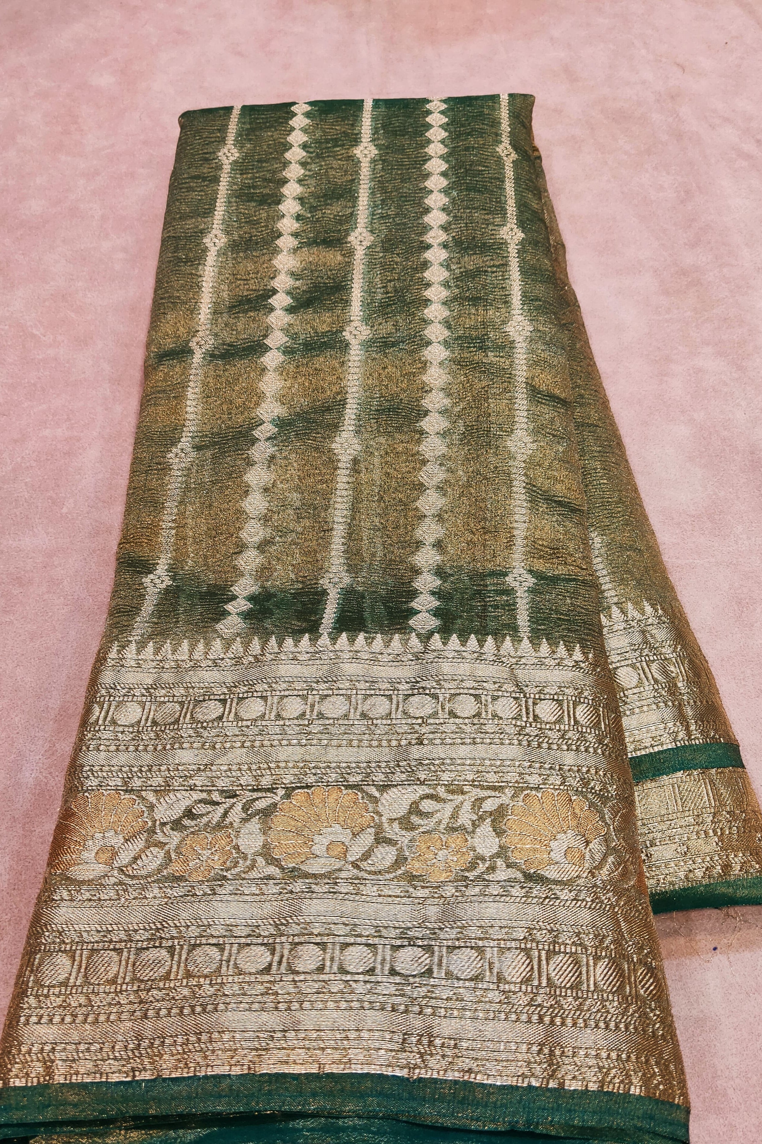 Green and gold patterned fabric held by a hand on a pink background