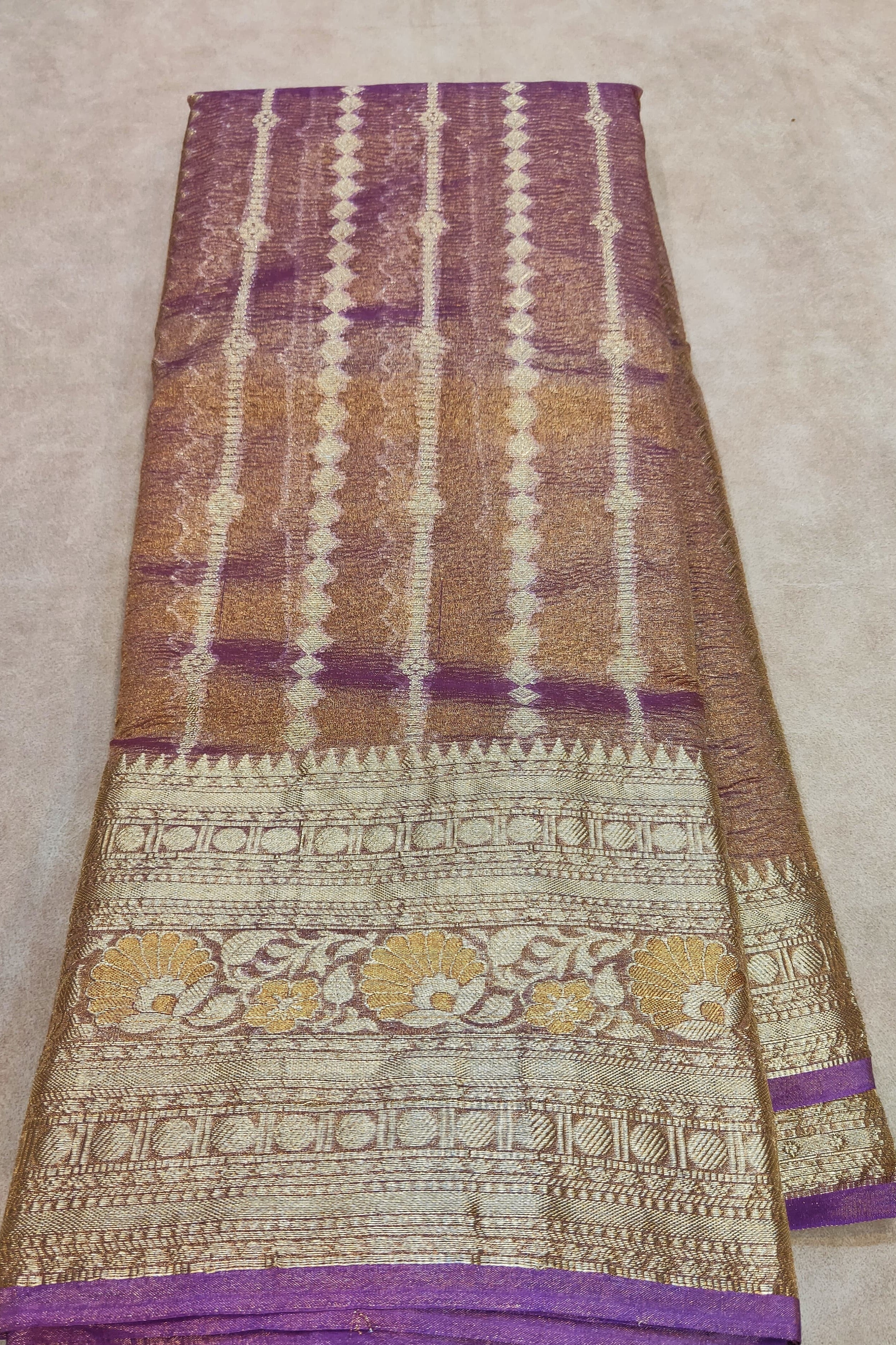 Folded fabric with purple, gold, and white pattern on a beige surface