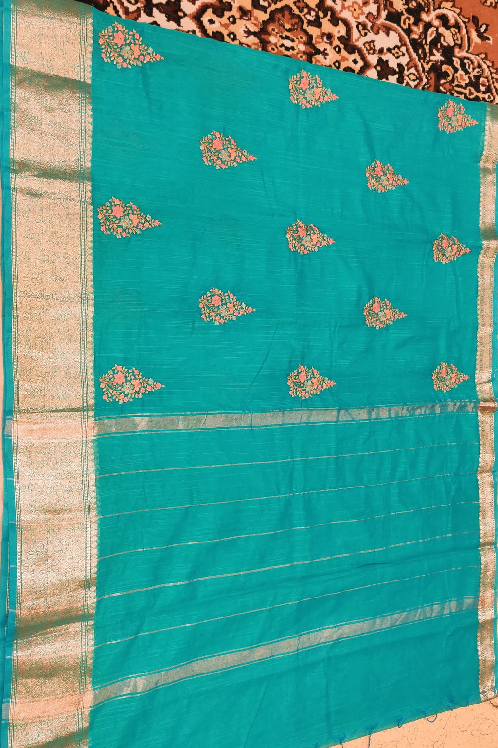 Teal saree with gold patterns on a patterned fabric background