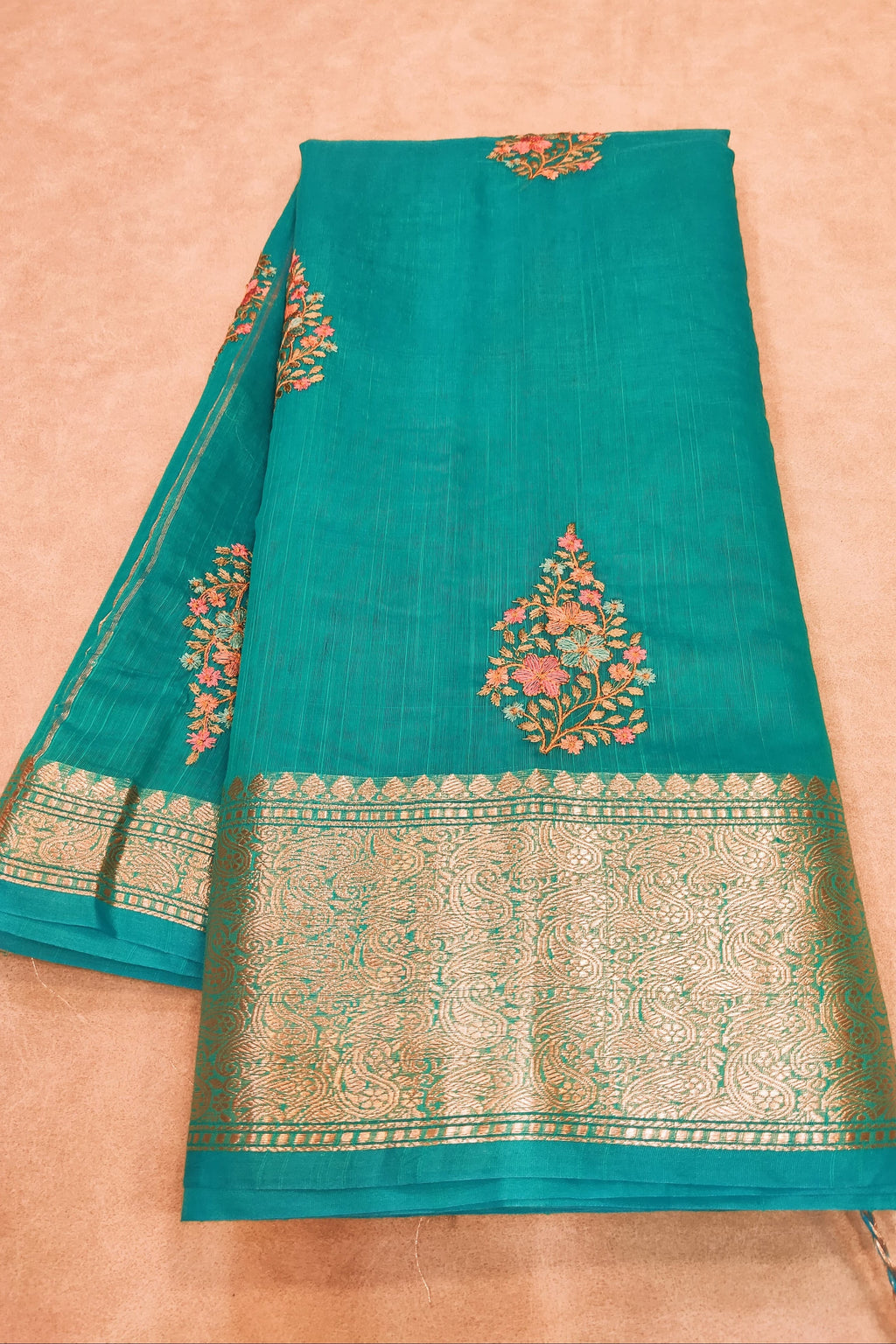Teal fabric with gold and red embroidery on a beige background