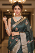 Woman in a green saree with floral patterns in an indoor setting