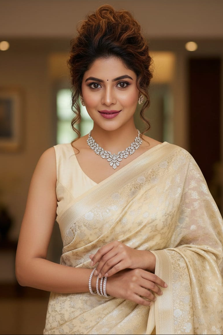 Woman in a cream saree with jewelry against a blurred indoor background