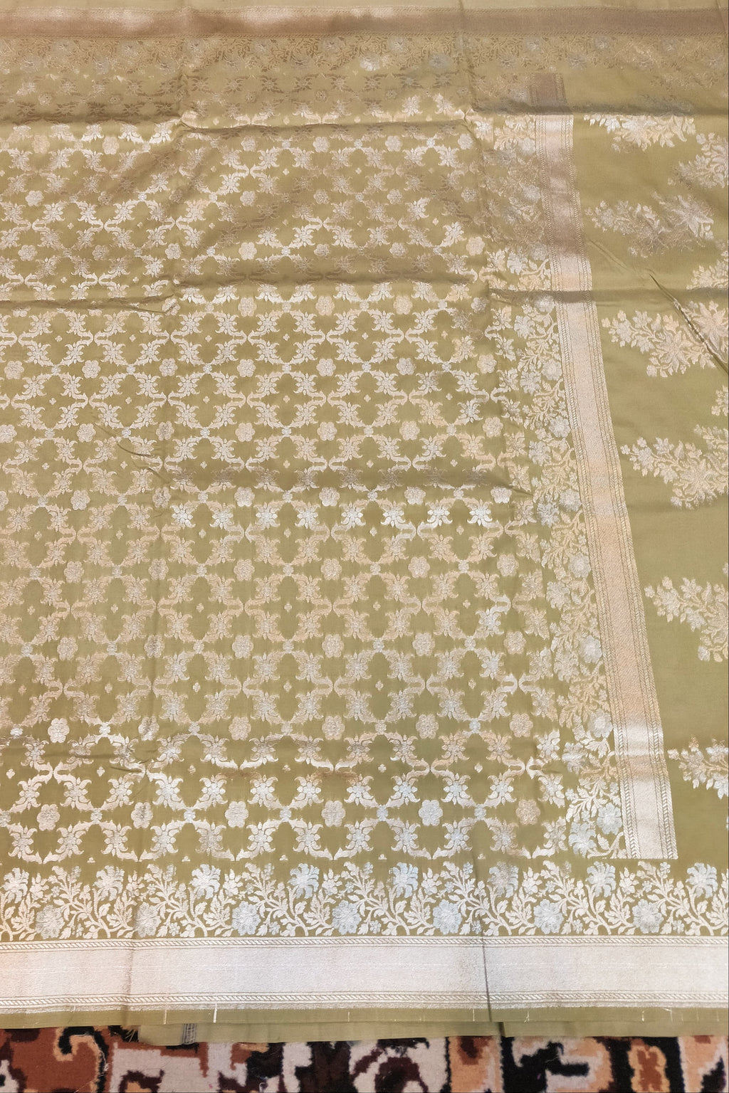 Green fabric with white floral patterns on a patterned carpet background