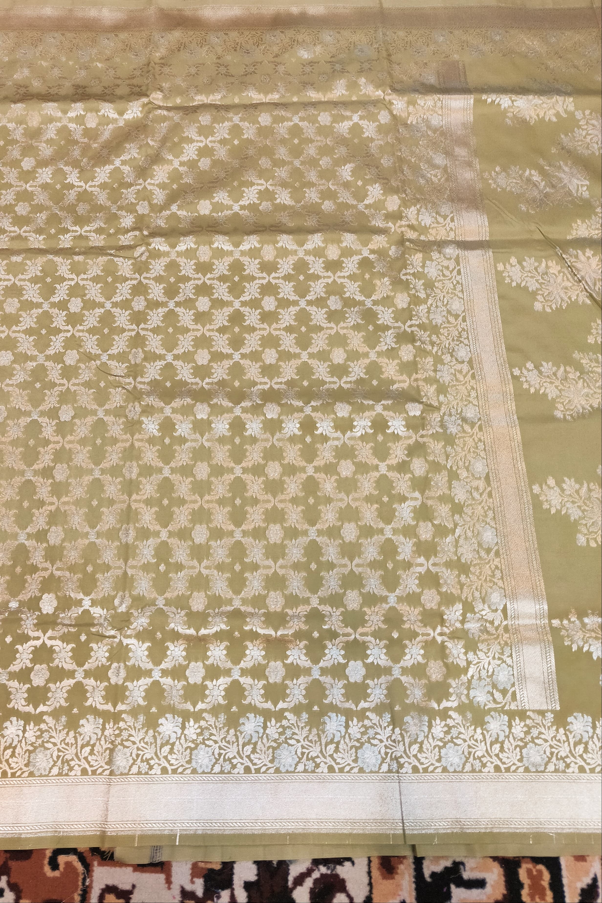 Green fabric with white floral patterns on a patterned carpet background