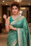 Woman in a green saree with a pattern, wearing jewelry indoors.