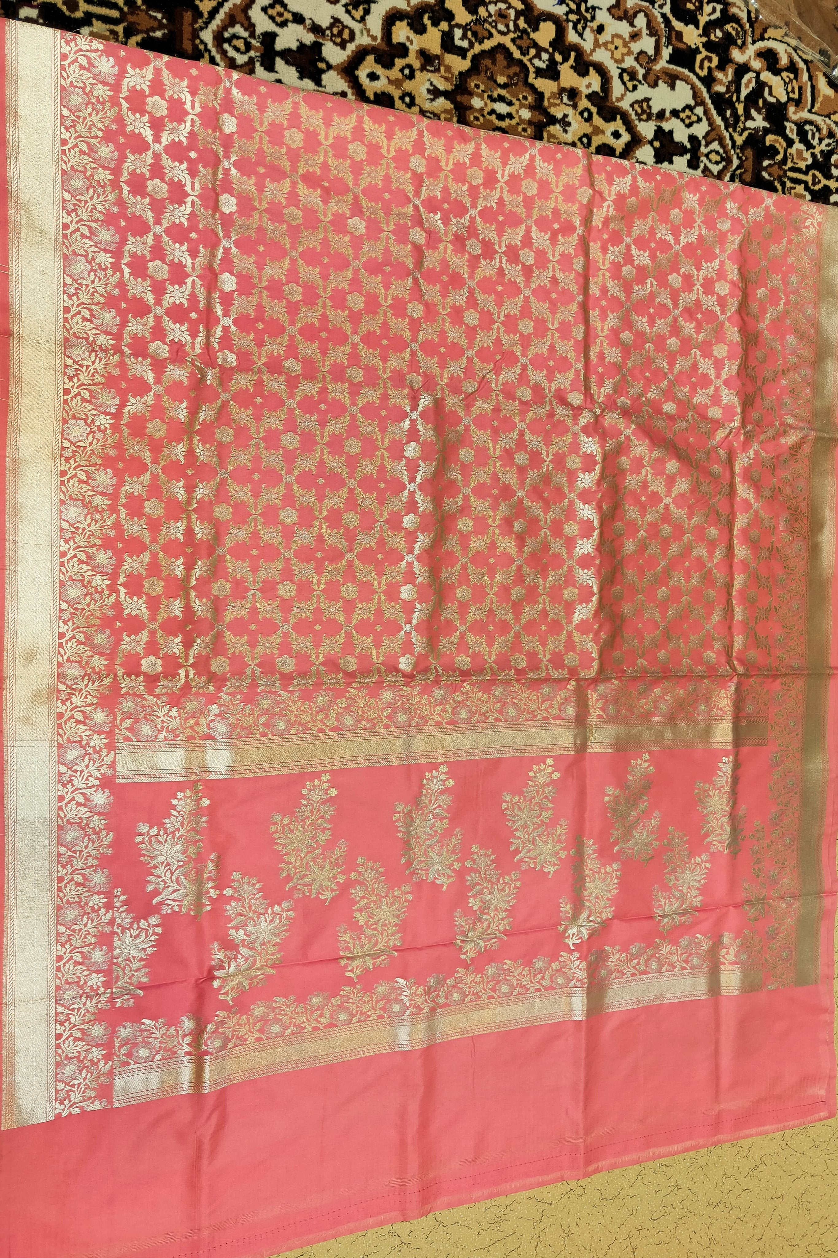 Pink saree with gold patterns on a patterned fabric background