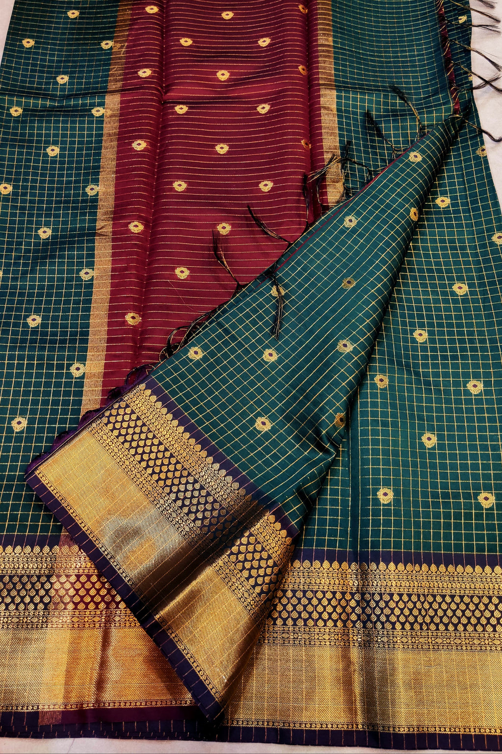 Green and maroon saree with gold patterns on a white surface