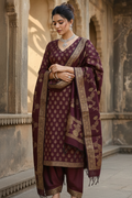Woman in traditional maroon outfit with gold patterns standing in an architectural setting.