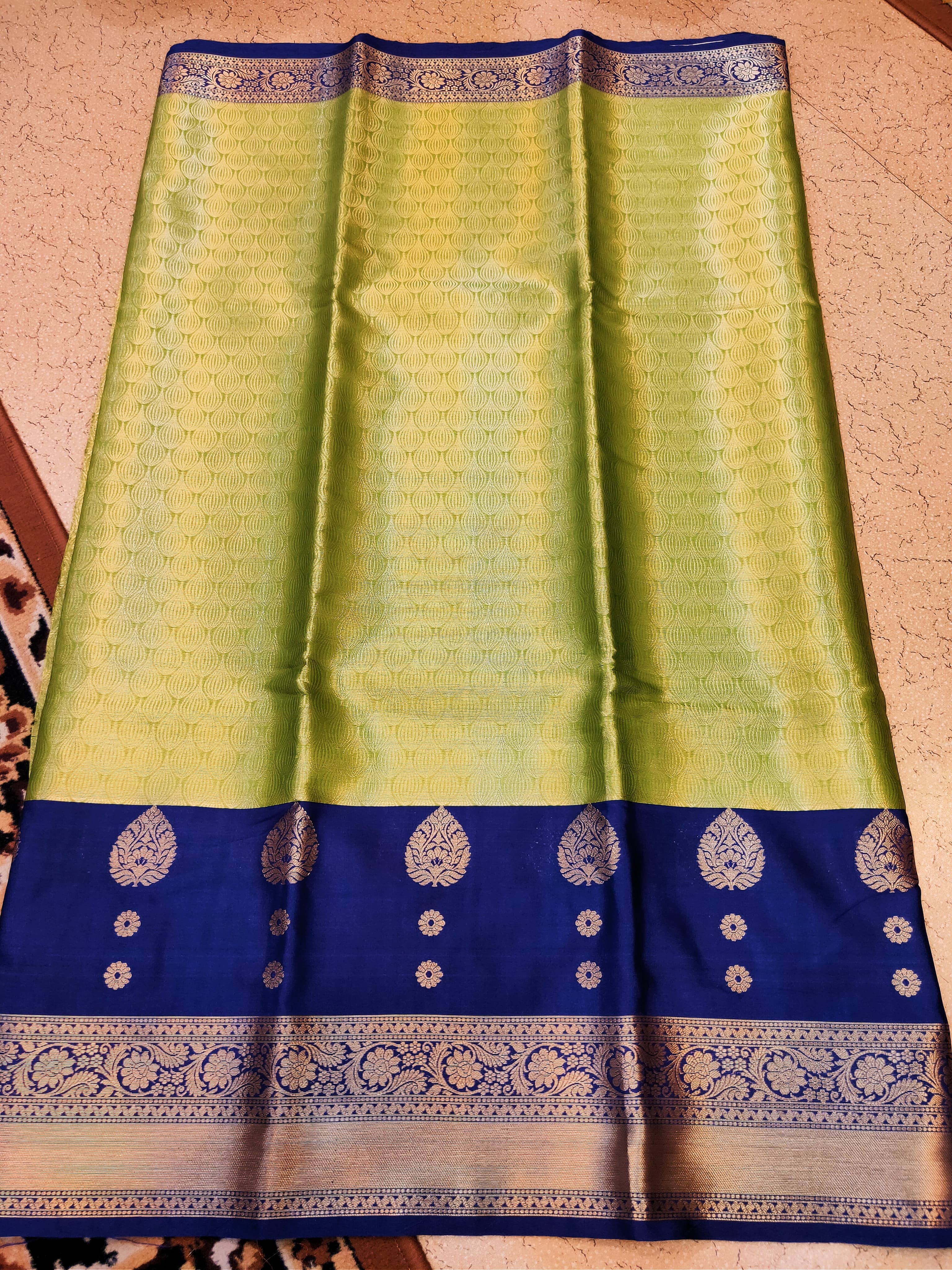 Green and blue saree with intricate patterns on a beige background