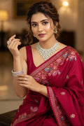 Woman in a red saree with intricate patterns, wearing jewelry, indoors.