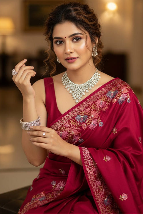 Woman in a red saree with intricate patterns, wearing jewelry, indoors.