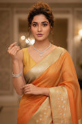 Woman wearing an orange saree with a gold border indoors.