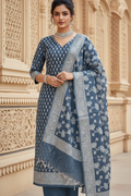 Woman wearing a blue and white patterned traditional outfit in front of an ornate architectural background.
