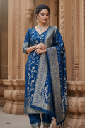 Woman in a blue traditional outfit with intricate patterns standing in front of architectural columns.