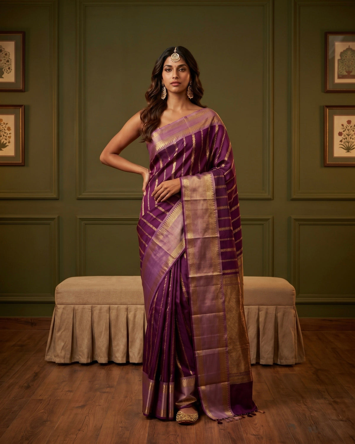 A woman models a purple and gold striped silk saree in an elegant room with olive green paneled walls and a wooden floor.