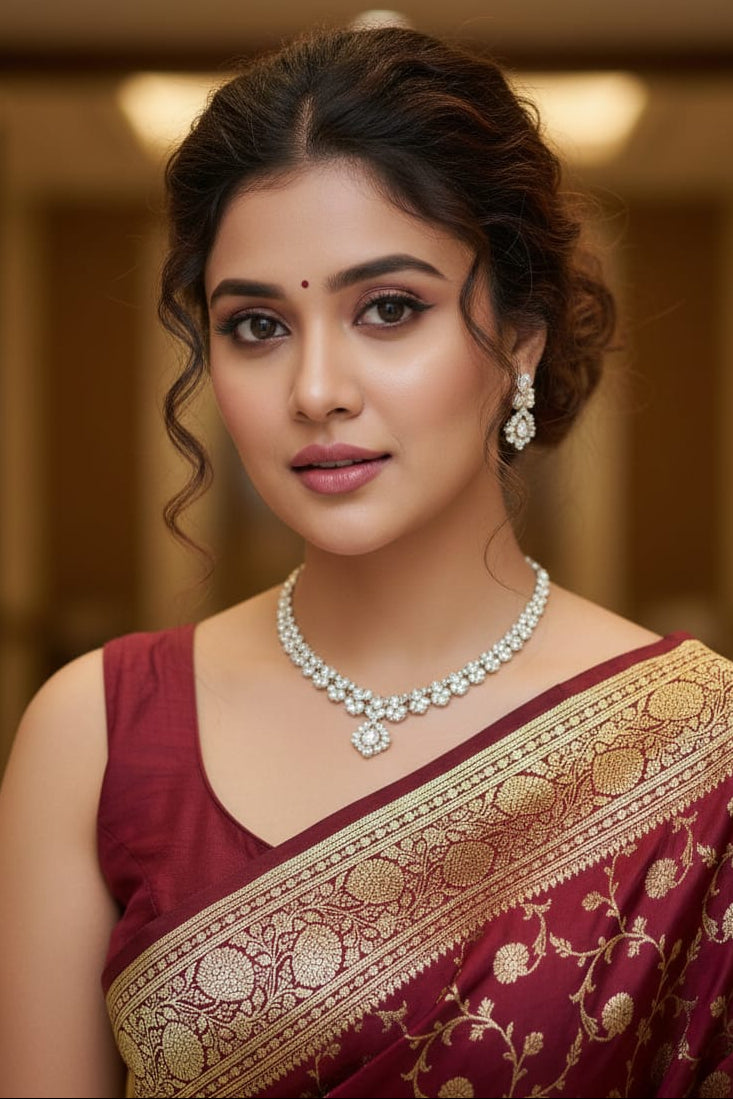Woman wearing a maroon saree with gold border and pearl jewelry indoors.