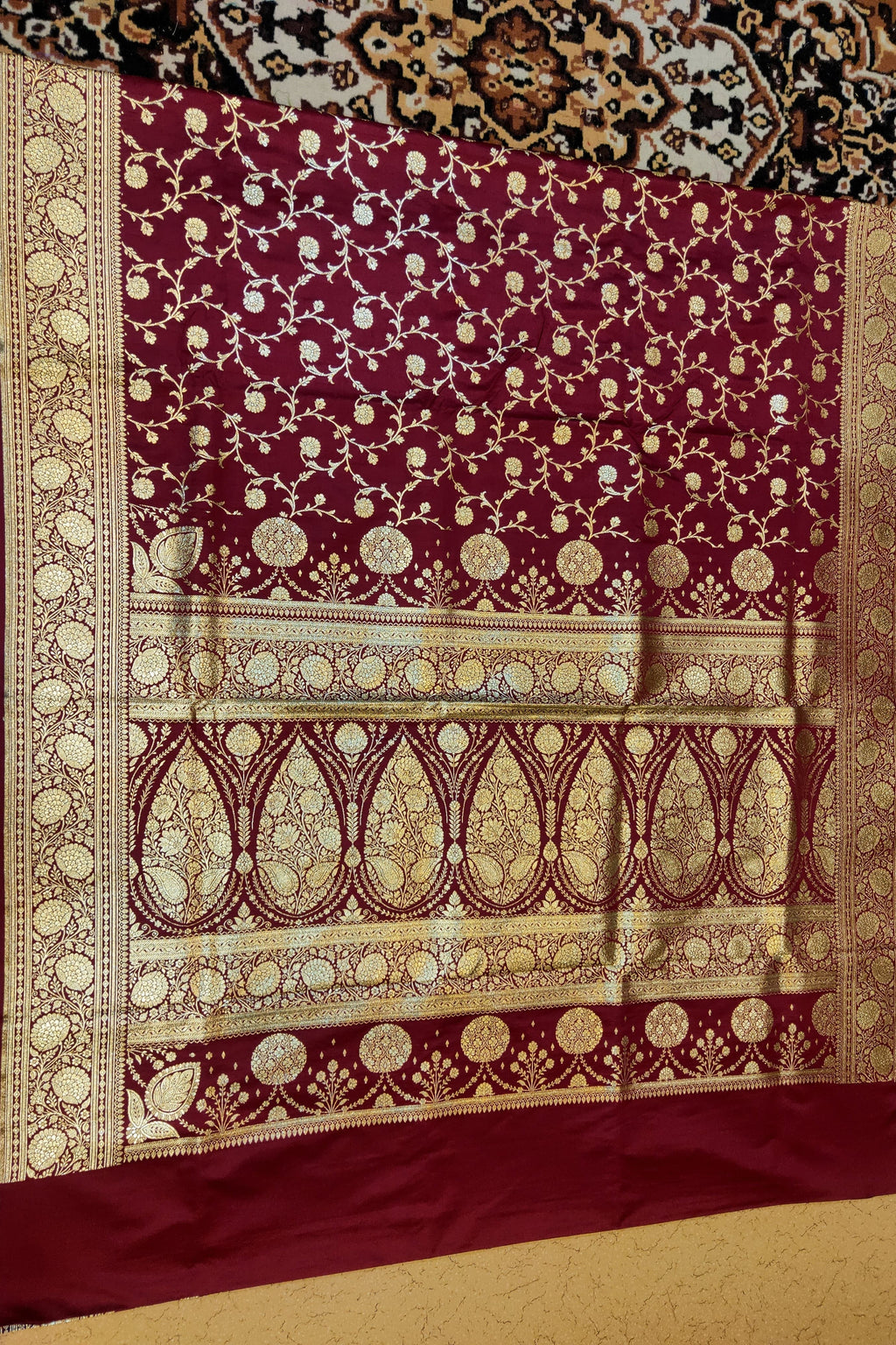 Decorative maroon fabric with gold patterns on a textured surface