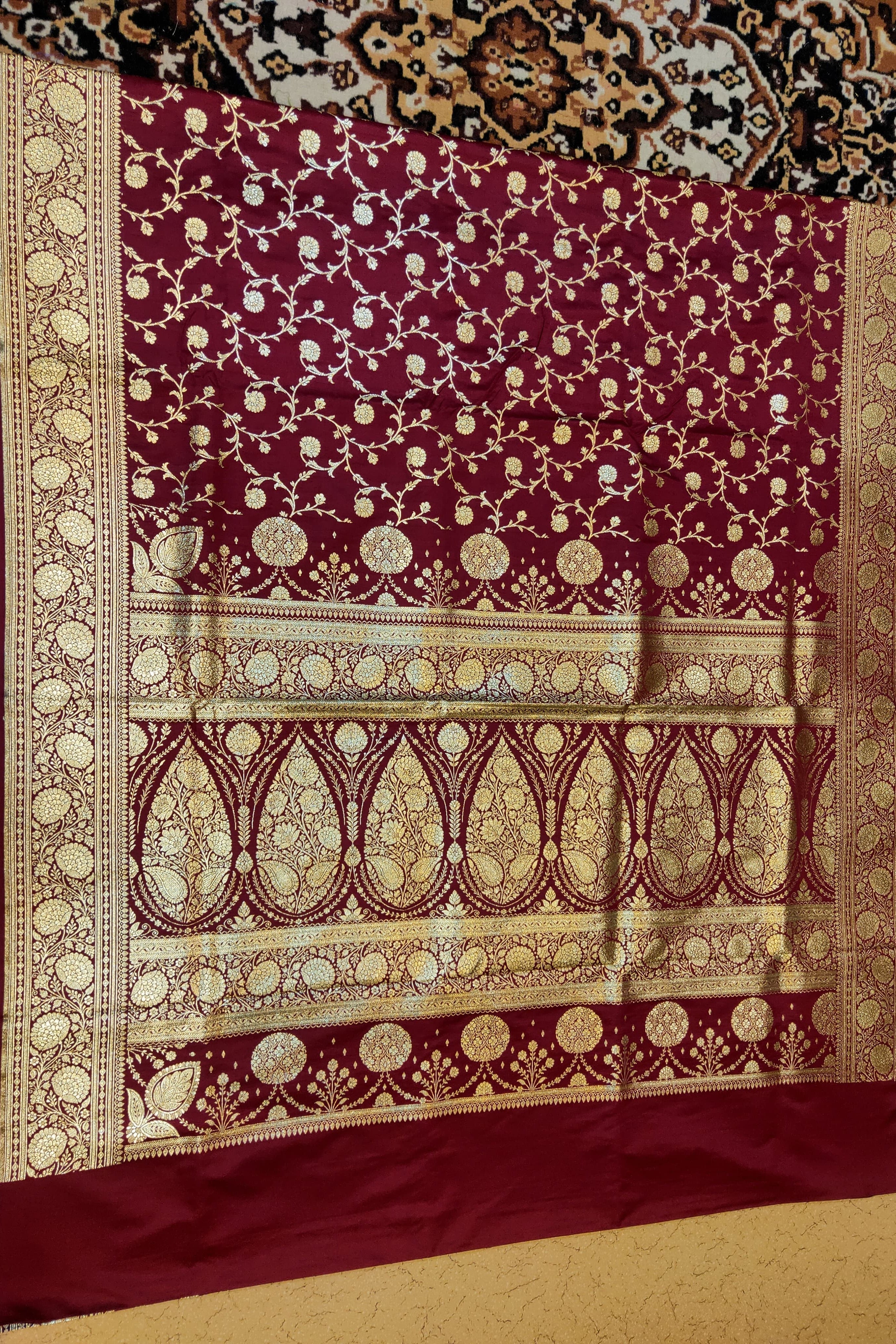 Decorative maroon fabric with gold patterns on a textured surface